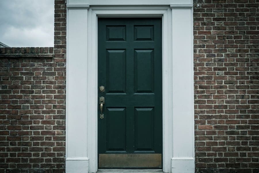 A deep green six panel wood front door with brass hardware.