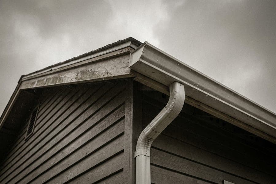 A white gutter and downspout corner against grey clapboard siding.