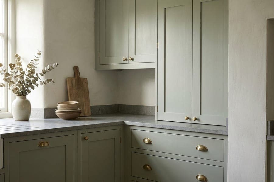 A corner of sage green shaker cabinets with a honed stone countertop.