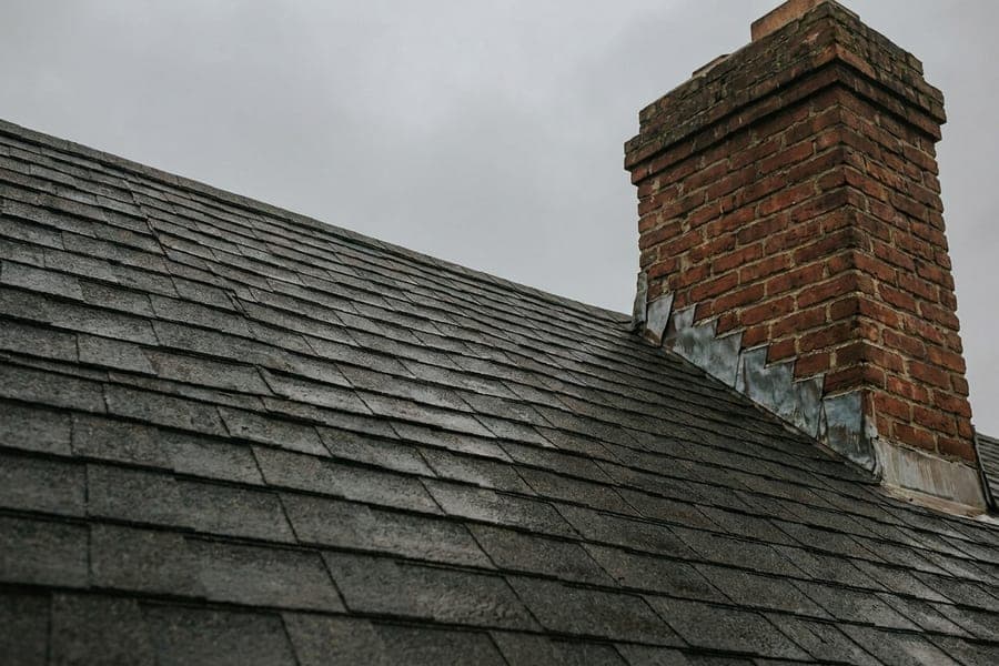 Dark grey architectural shingles on a steep roof beside a brick chimney.