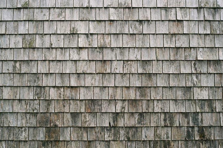 Overlapping courses of silver grey weathered cedar shingle siding.