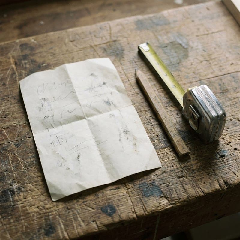 A folded paper estimate on a wooden surface with a carpenter's pencil and tape measure.